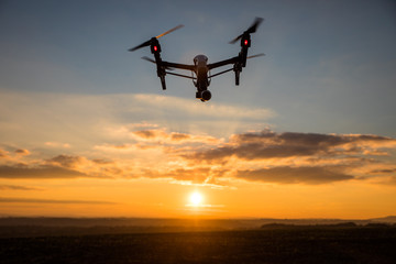 Fototapeta na wymiar White drone with digital camera flying in sky over field on sunset