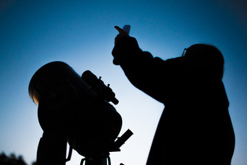 Astronomer and his astronomical telescope at night in front of the sky