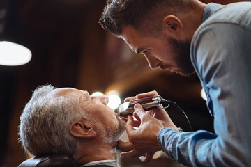 Side view of young barber trimming beard