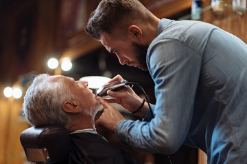 Side view of young barber trimming beard