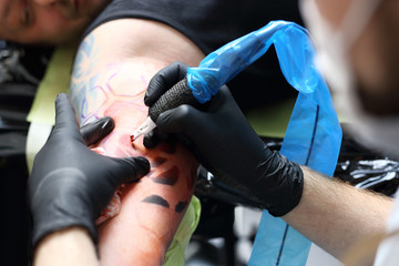 Tatuaż,tatuator wykonuje tatuaż na ręce mężczyzny