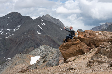 Tourist with a backpack sitting on top of  mountain and taking pictures  the phone. The height  3000 meters.