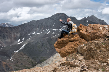 Tourist with a backpack sitting on top of  mountain and taking pictures  the phone. The height  3000 meters.