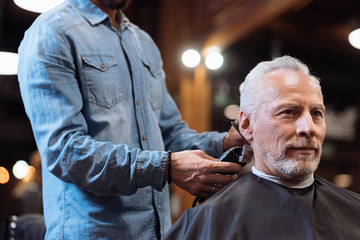 Close up barber trimming hair of old man