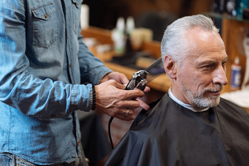 Close up barber trimming hair of old man