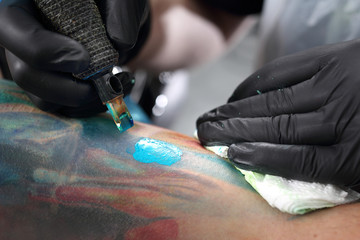 Maszynka do tatuażu. Tatuator tatuuje kolorowy tatuaż na ręku mężczyzny © Robert Przybysz