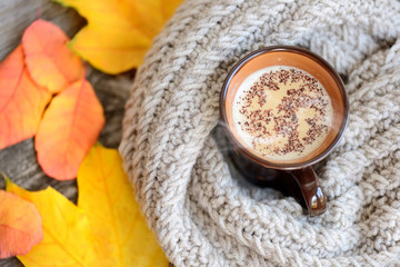 Autumn leaves, hot cup of coffee and a warm scarf on wooden table background
