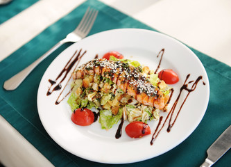 Salad with salmon on a white plate. Served on a table with a green tablecloth in a restaurant
