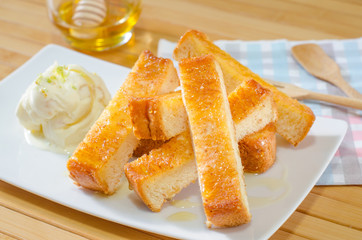 Close-up, Toast topped with honey butter serve with ice cream, cut into sticks arranged on a white plate. Background have wooden spoon fork, honey dipper with honey. There is space for add decoration.