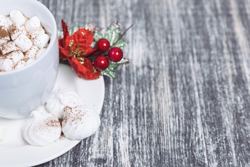 Hot chocolate with marshmallows. Drink in a white ceramic cup with zephyr on wooden table. Red poinsettia flower on plate, saucer. Copy space