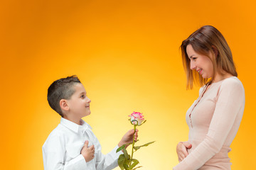 Young kid giving red rose to his mom