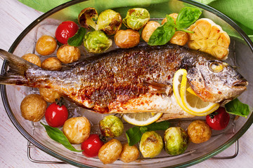 Roasted dorado fish with brussels sprouts, tomatoes, garlic, young potato and greens. View from above, top studio shot
