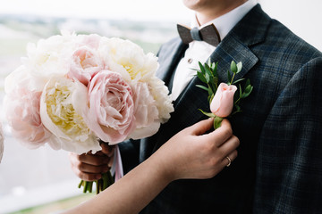 Bride puts on to the groom boutonniere. Beautiful bouquet of pink peonies, close up