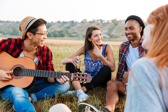 Smiling young friends drinking beer and playing guitar outdoors
