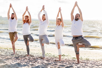 Obraz premium people making yoga in tree pose on summer beach