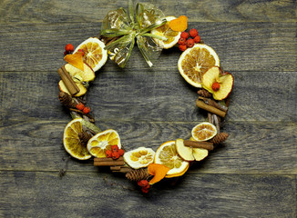 Fototapeta na wymiar Christmas hand made craft on old wooden background. Traditional New Year`s door wreath components from dried oranges, cones. Big Copyspace frame for logo and text.