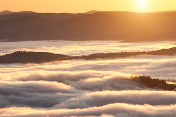 Summer weather phenomenon. Seasonal landscape with morning fog in valley. Clouds drenched valley below the level of the mountains. Sunrise over creeping clouds.