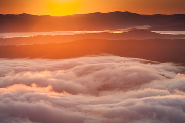 Summer weather phenomenon. Seasonal landscape with morning fog in valley. Clouds drenched valley below the level of the mountains. Sunrise over creeping clouds.
