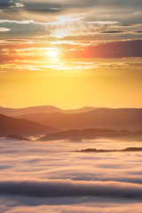 Summer weather phenomenon. Seasonal landscape with morning fog in valley. Clouds drenched valley below the level of the mountains. Sunrise over creeping clouds.