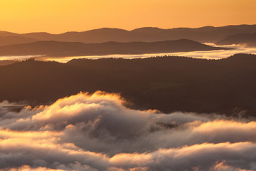Summer weather phenomenon. Seasonal landscape with morning fog in valley. Clouds drenched valley below the level of the mountains. Sunrise over creeping clouds.