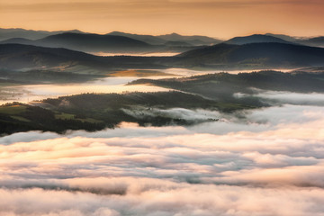 Summer weather phenomenon. Seasonal landscape with morning fog in valley. Clouds drenched valley below the level of the mountains. Sunrise over creeping clouds.