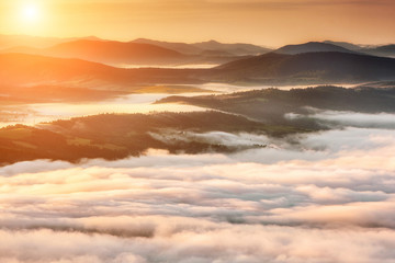Summer weather phenomenon. Seasonal landscape with morning fog in valley. Clouds drenched valley below the level of the mountains. Sunrise over creeping clouds.