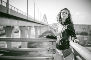 portrait of a beautiful young woman with long thin hair, a leather jacket, blue jeans. warm autumn sunny day on the stairs of the bridge.