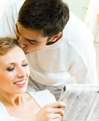 Obraz premium Young happy amorous couple reading newspaper at home. Love, relations, romantic concept shoot.