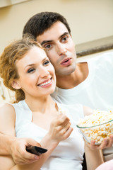 Young couple eating popcorn and watching TV together at home. Love, relations, romantic concept shoot.