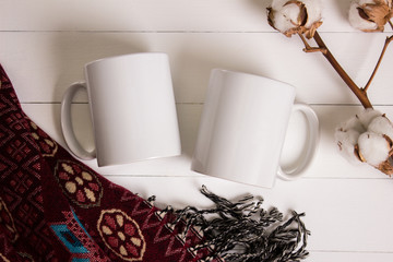 Two white mugs, pair of cups, Mockup. Cozy atmosphere, wooden background, cotton and wool decorations for winter gifts.
