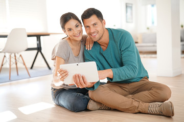 Couple connected on digital tablet, sitting on floor