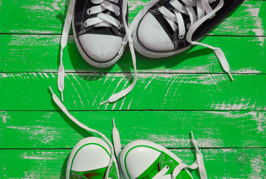 Two pairs of sneakers youth with untied laces on the green surfa