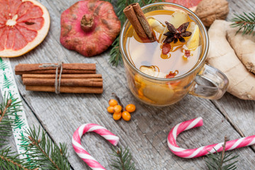 Christmas composition. Spruce branches, candy cane, warming tea with ginger and lemon,  dried oranges, grapefruit, cinnamon, star anise, pomegranates on a wooden background.