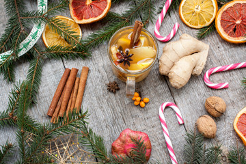 Fototapeta na wymiar Christmas composition. Spruce branches, candy cane, warming tea with ginger and lemon, dried oranges, grapefruit, cinnamon, star anise, pomegranates on a wooden background.