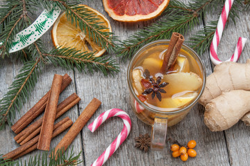 Christmas composition. Spruce branches, candy cane, warming tea with ginger and lemon,  dried oranges, grapefruit, cinnamon, star anise, pomegranates on a wooden background.