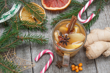 Obraz na płótnie Canvas Christmas composition. Spruce branches, candy cane, warming tea with ginger and lemon, dried oranges, grapefruit, cinnamon, star anise, pomegranates on a wooden background.