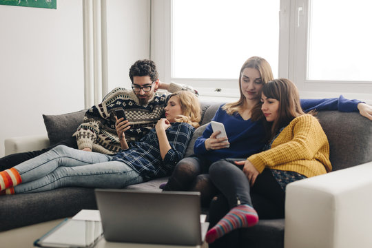 Four friends with smartphones on couch in living room hanging out