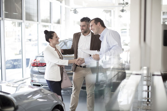 Car dealer shaking hands with woman in car dealership