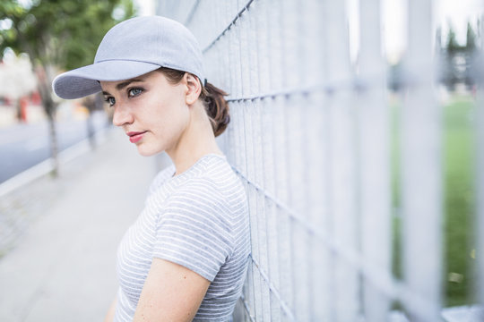 Portrait of woman wearing baseball cap leaning against fence