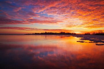 Fototapeta na wymiar Beautiful winter landscape with sunset fiery sky and frozen lake