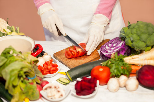 Woman with gloves slicing tomato on chopping board