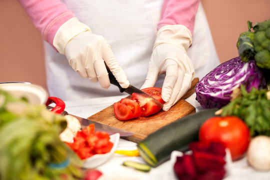 Woman with gloves slicing tomato with a knife in the kitchen