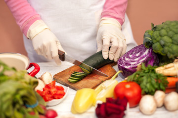 Woman with white glove cutting cucumber in the kitchen