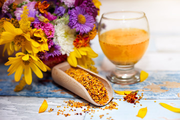 Bee pollen in glass and wooden scoop with colorful flowers in th