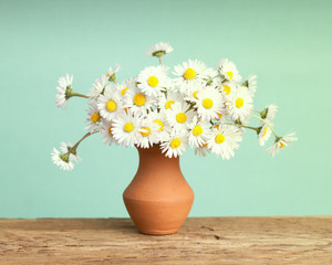 Retro daisy's flowers in a brown ceramic pot on a solid wood surface © iLight photo