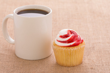 Coffee cup with a strawberry flavored cupcake, on burlap background