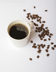 Black coffee on a white mug next to coffee beans.