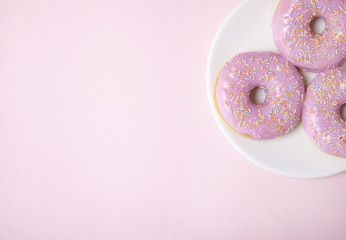 A plate of pastel colored ring doughnuts with sprinkles on a pink background with blank space at side