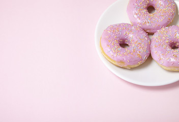 A plate of ring donuts with pastel pink frosting and sprinkles on a colorful background with blank space at side