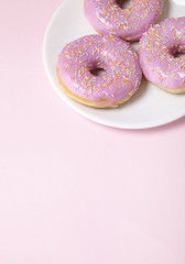 A plate of ring donuts with pastel pink frosting and sprinkles on a colorful background with blank space below